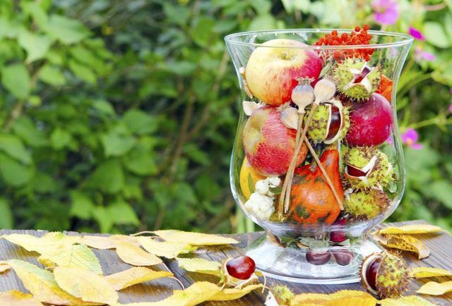 Un vase en verre rempli de fruits et de fleurs de saison.